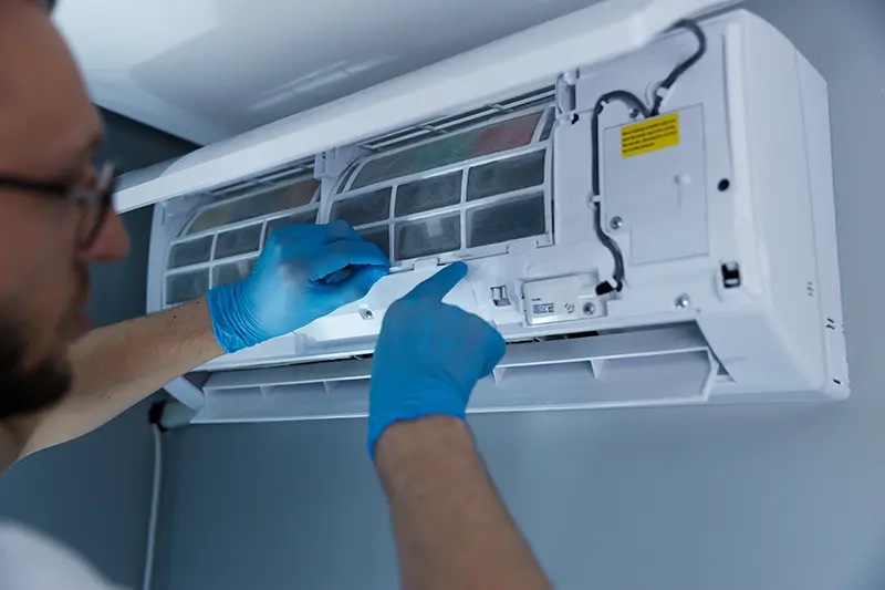 Man wearing gloves performing maintenance on mini-split AC Unit